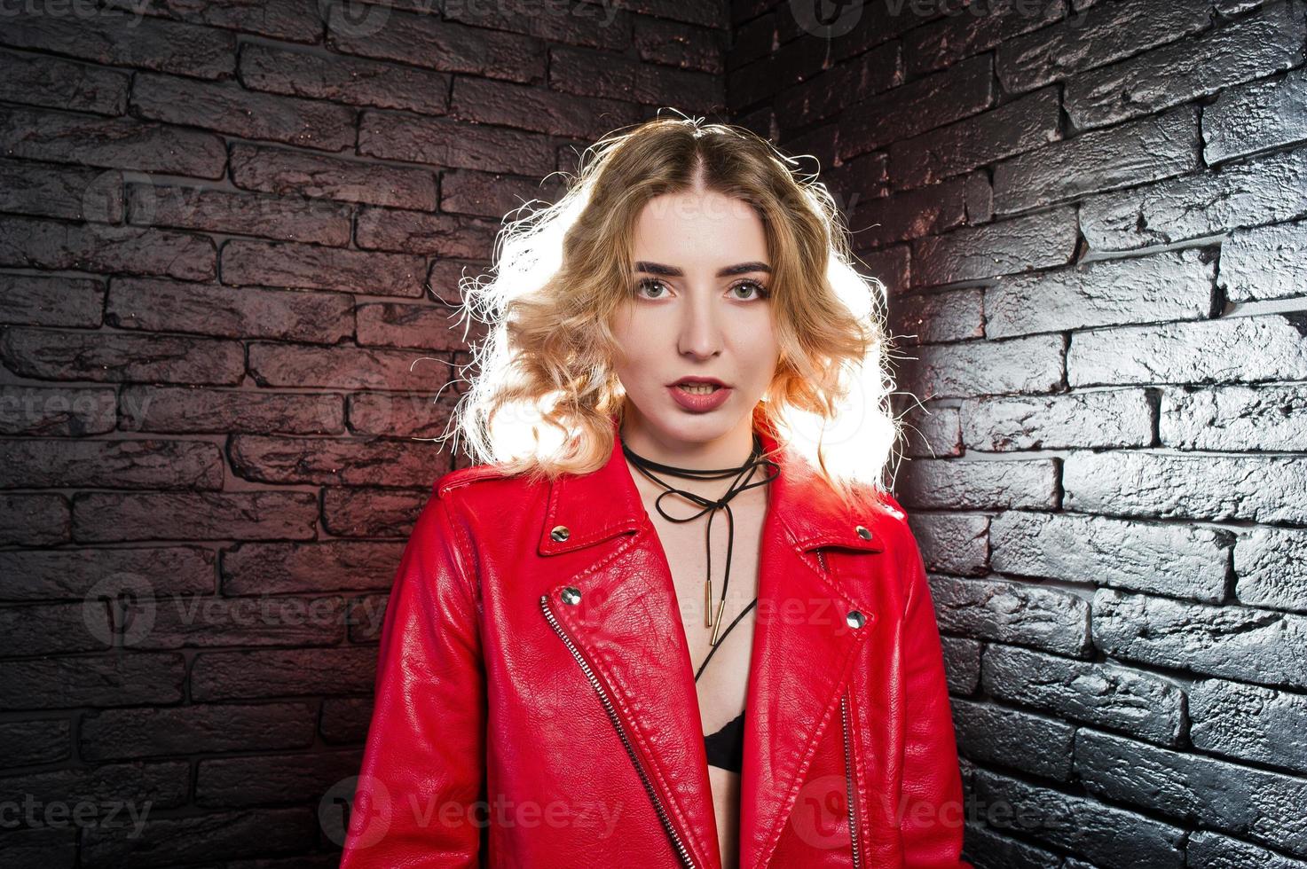 retrato de estudio de una chica rubia con una chaqueta de cuero roja contra una pared de ladrillos. foto