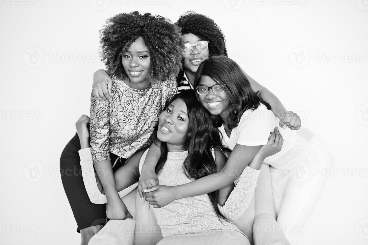 felices y brillantes momentos positivos de cuatro niñas africanas. divirtiéndose y sonriendo en una silla contra una pared blanca vacía. momentos encantadores de cuatro mejores amigos abrazando. foto
