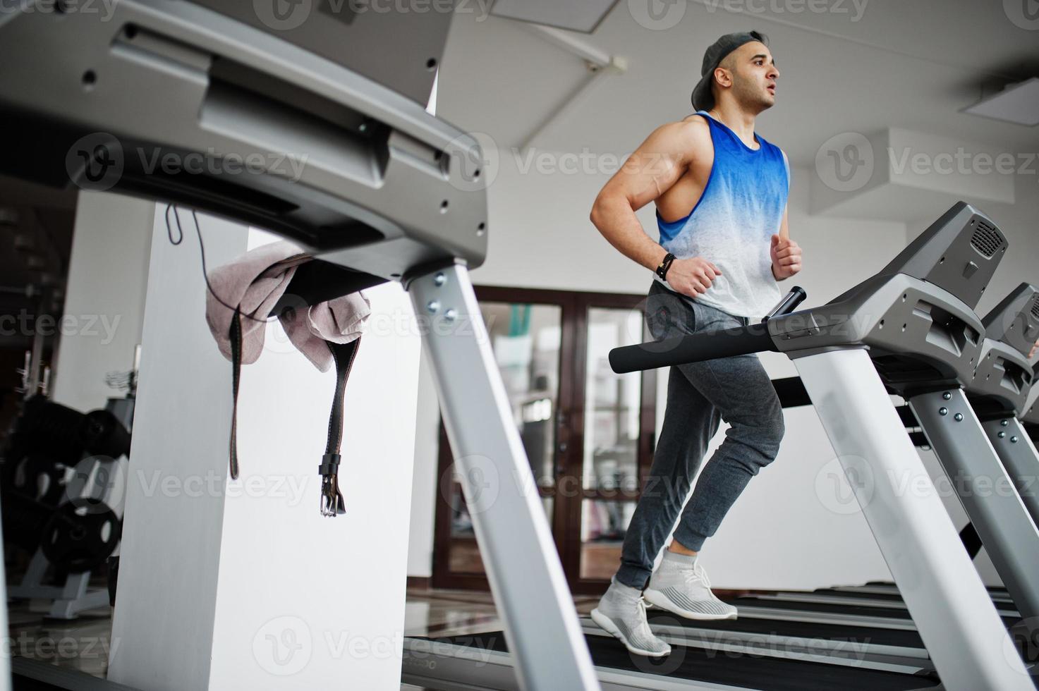 Fit and muscular arabian man running on treadmill in gym. photo