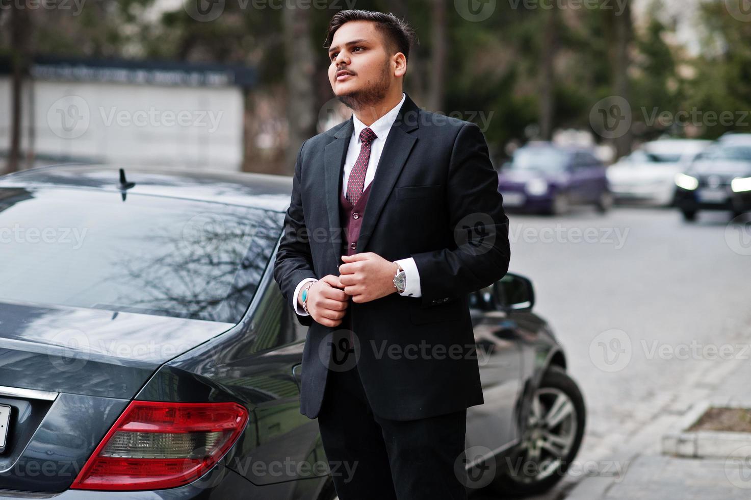 Stylish indian businessman in formal wear standing against black business car on street of city. photo
