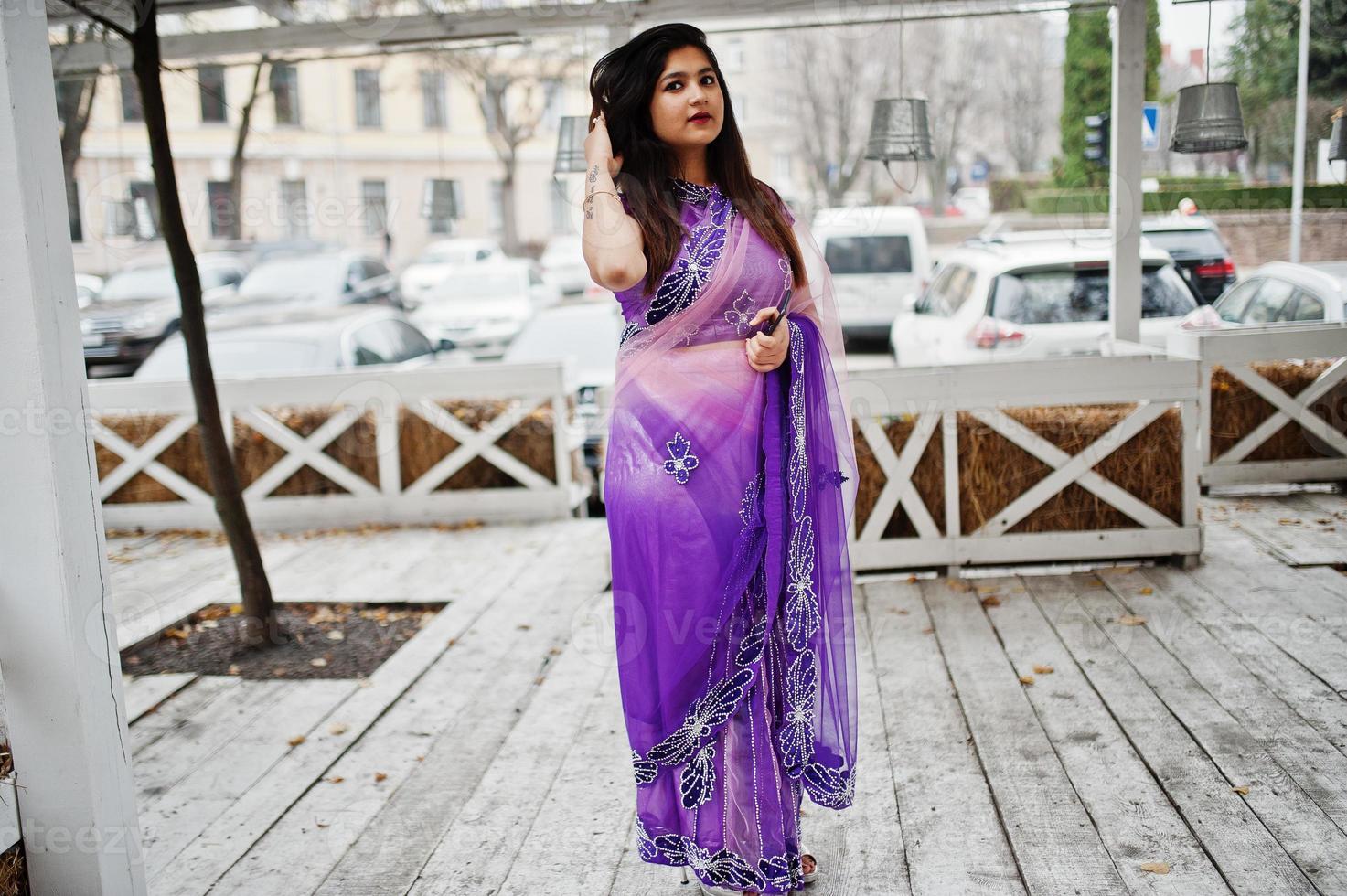 Indian hindu girl at traditional violet saree posed at street against wooden terrace. photo