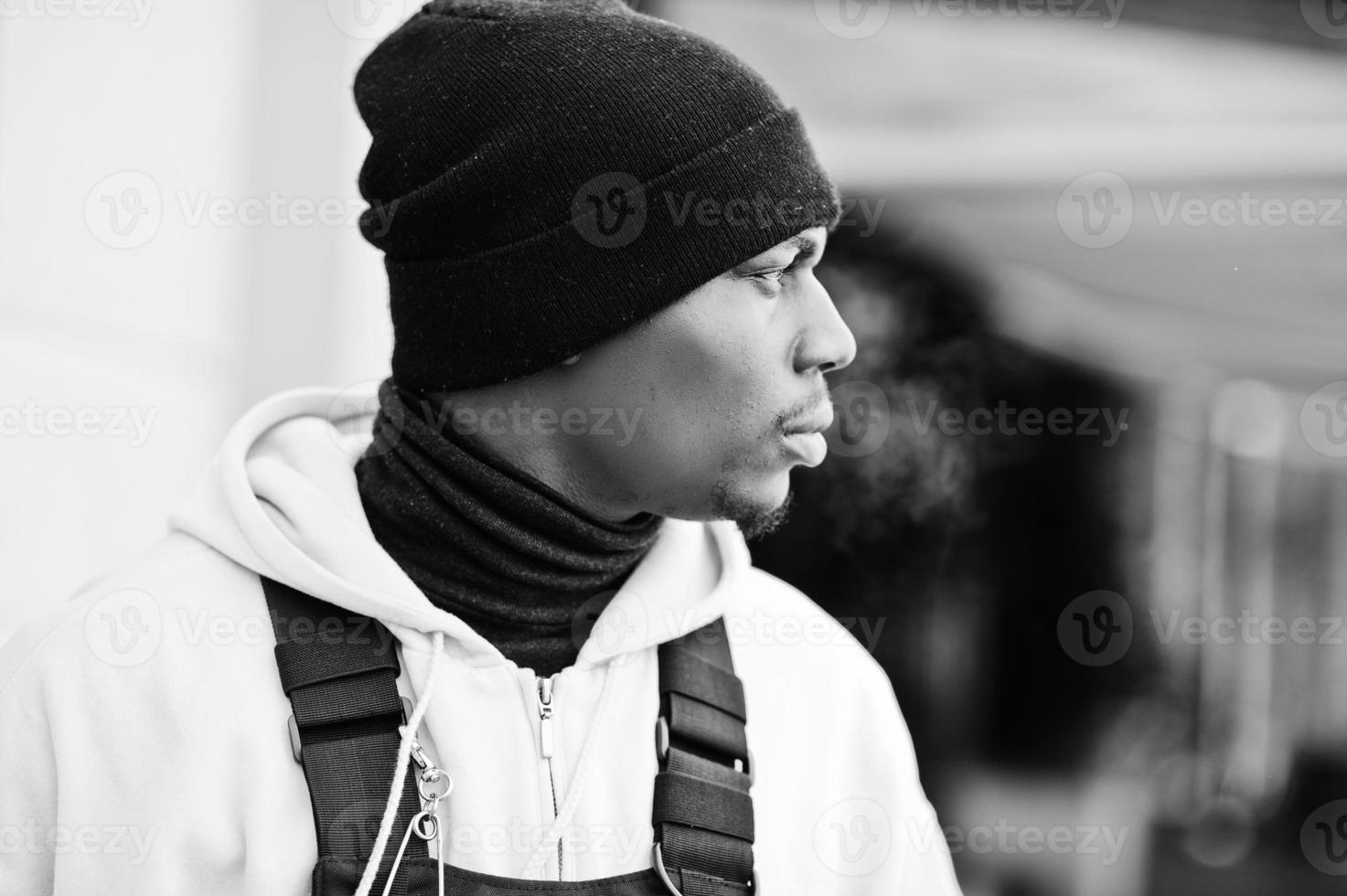 Close up head of stylish urban style african american man in pink hoodie and black hat posed. Frozen breath. photo