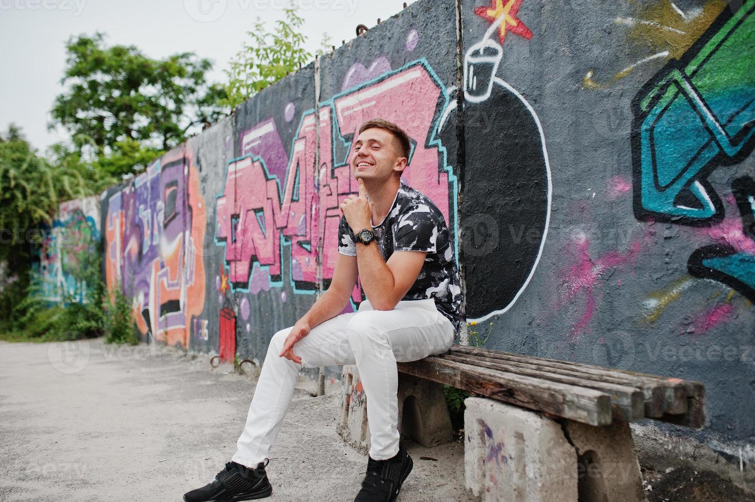 retrato de estilo de vida de un hombre guapo posando en la calle de la ciudad con una pared de graffiti. foto