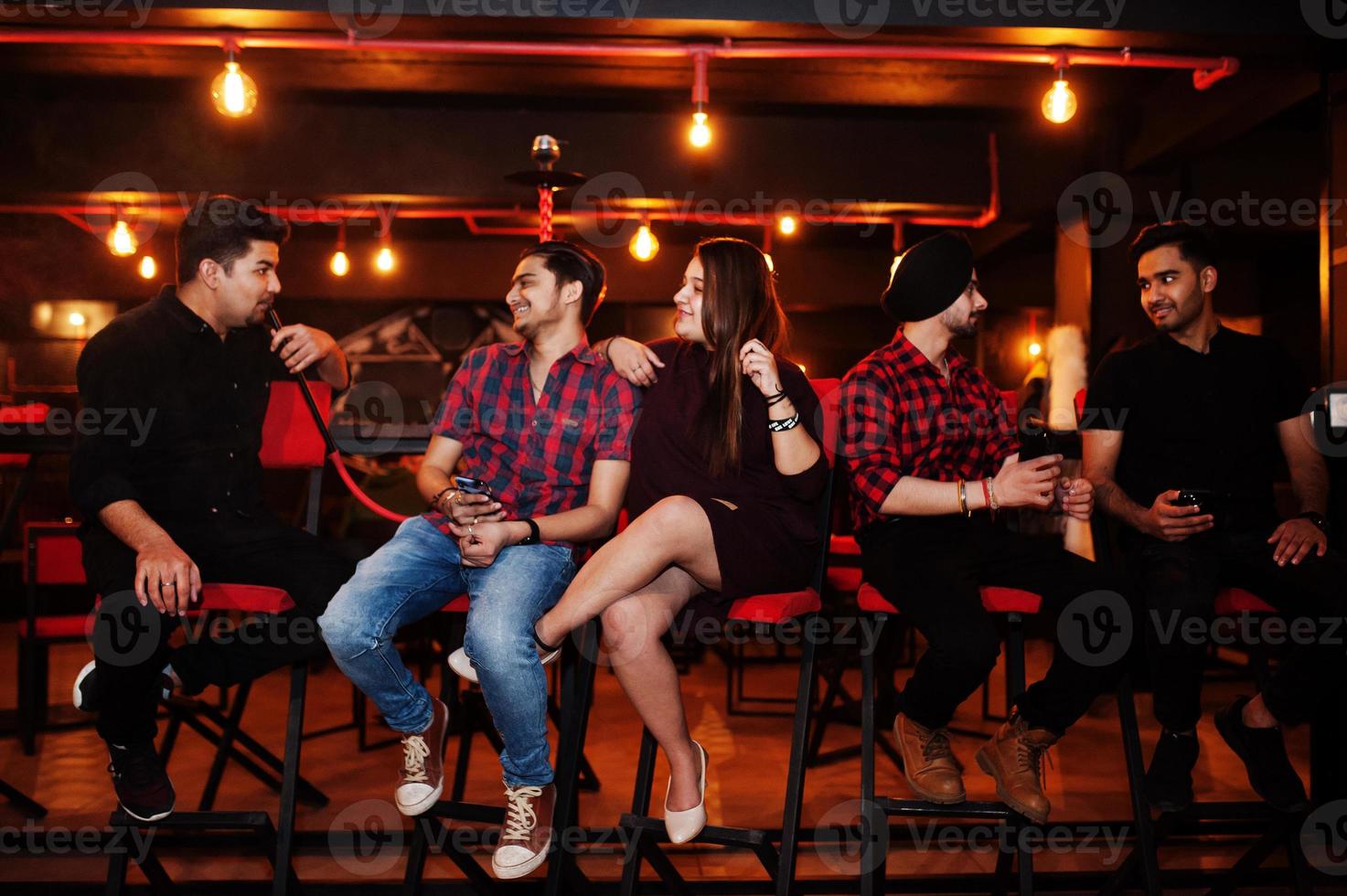 Group of indian friends sitting at lounge bar, smoke hookah and having rest. photo