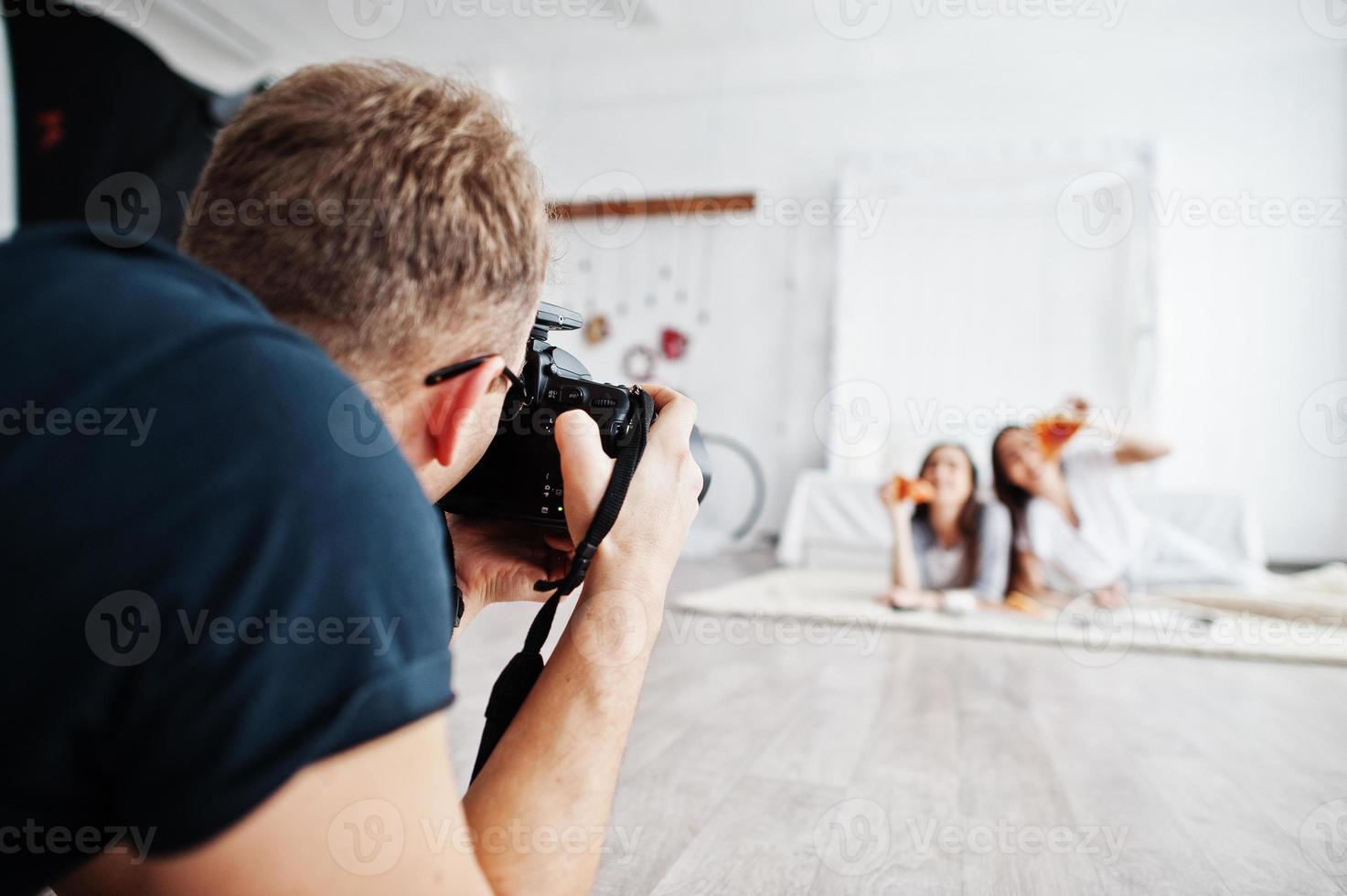 Man photographer shooting on studio twins girls who are eating pizza. Professional photographer on work. photo