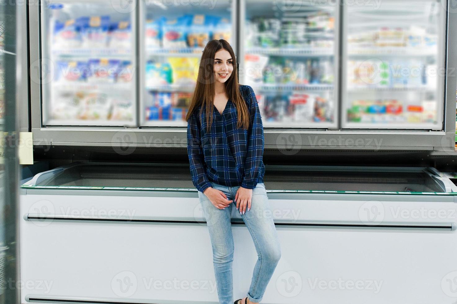 Shopping woman looking at the shelves in the supermarket.  Portrait of a young girl in a market store taking seafood from fridge. photo