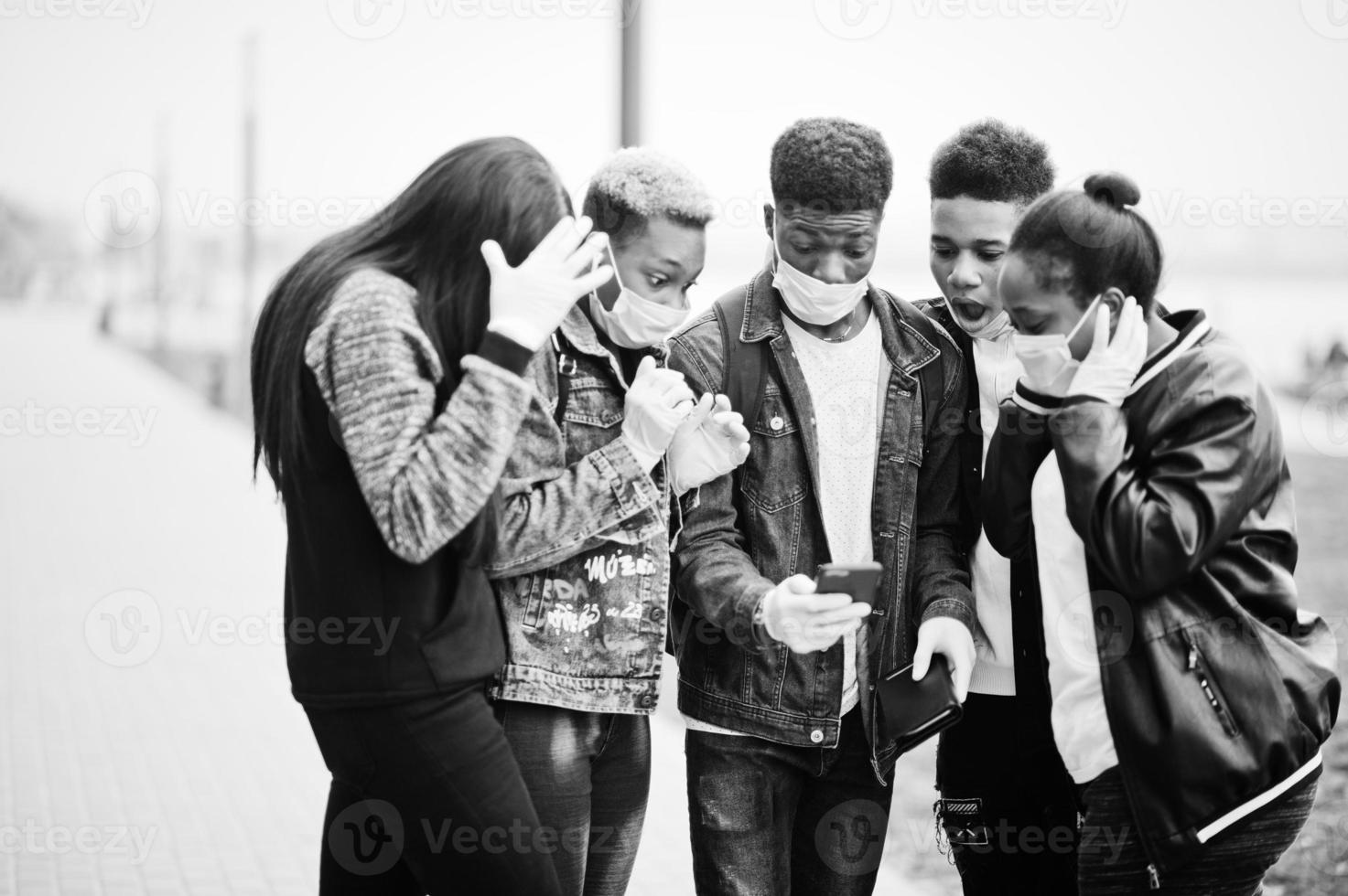 Group of african teenagers friends at park wearing medical masks protect from infections and diseases coronavirus virus quarantine, read shocked news on phone. photo