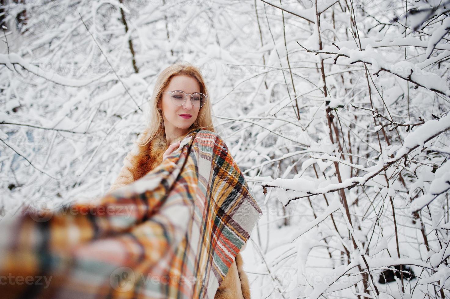 Portraiy of blonde girl in glasses, red fur coat and scarf at winter day. photo