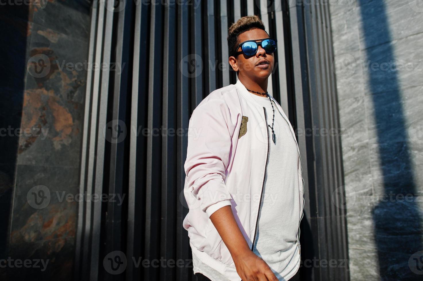 Stylish hipster arab man guy in sunglasses posed outdoor in street at sunset against gray wall. photo