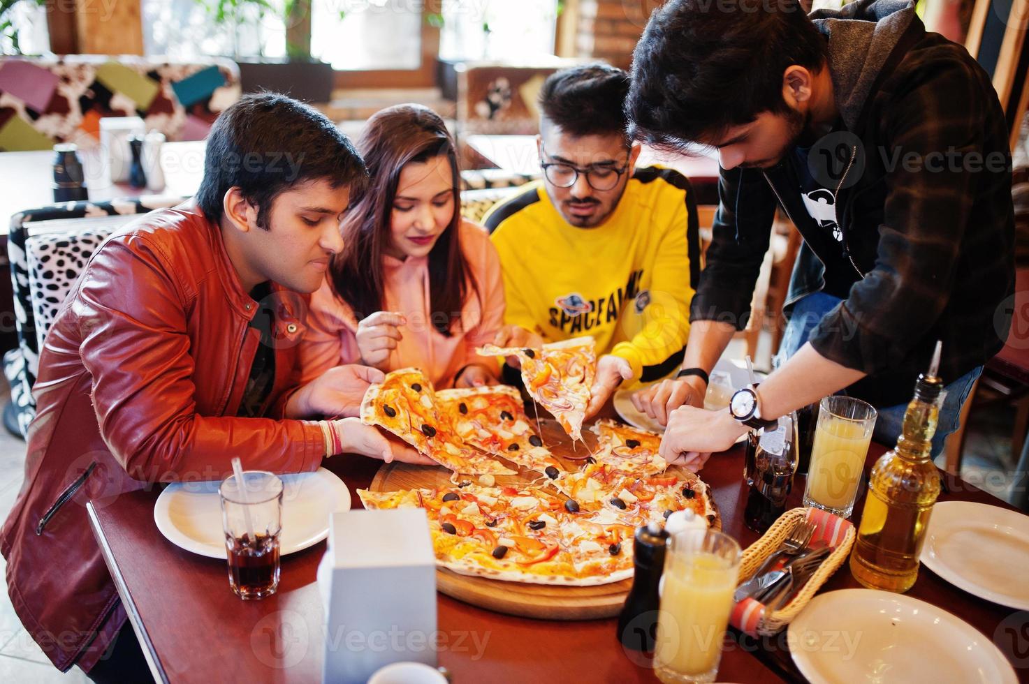 Group of asian friends eating pizza during party at pizzeria. Happy indian people having fun together, eating italian food and sitting on couch. photo
