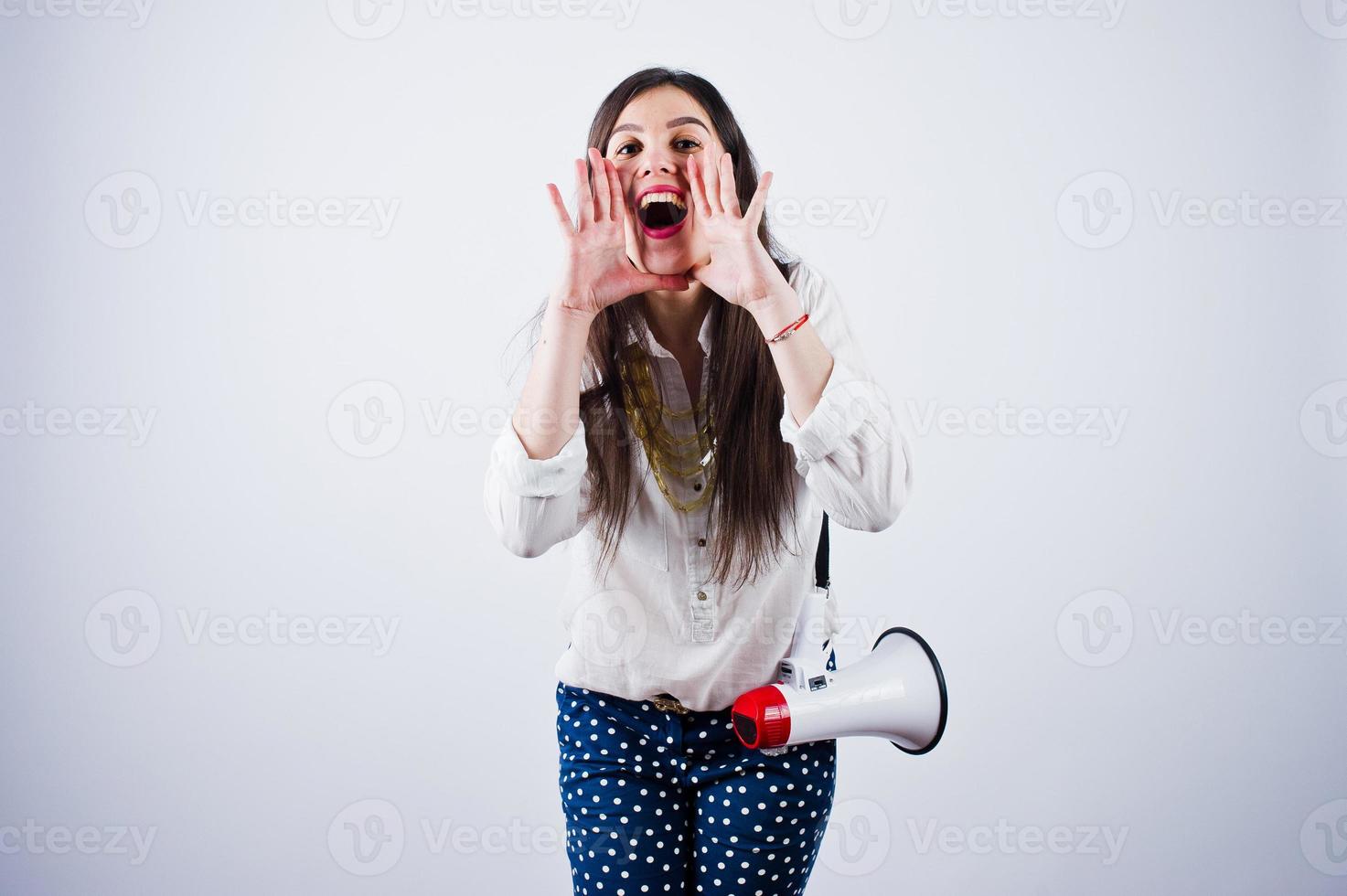 Portrait of a young woman in blue trousers and white blouse posing with megaphone in the studio. photo