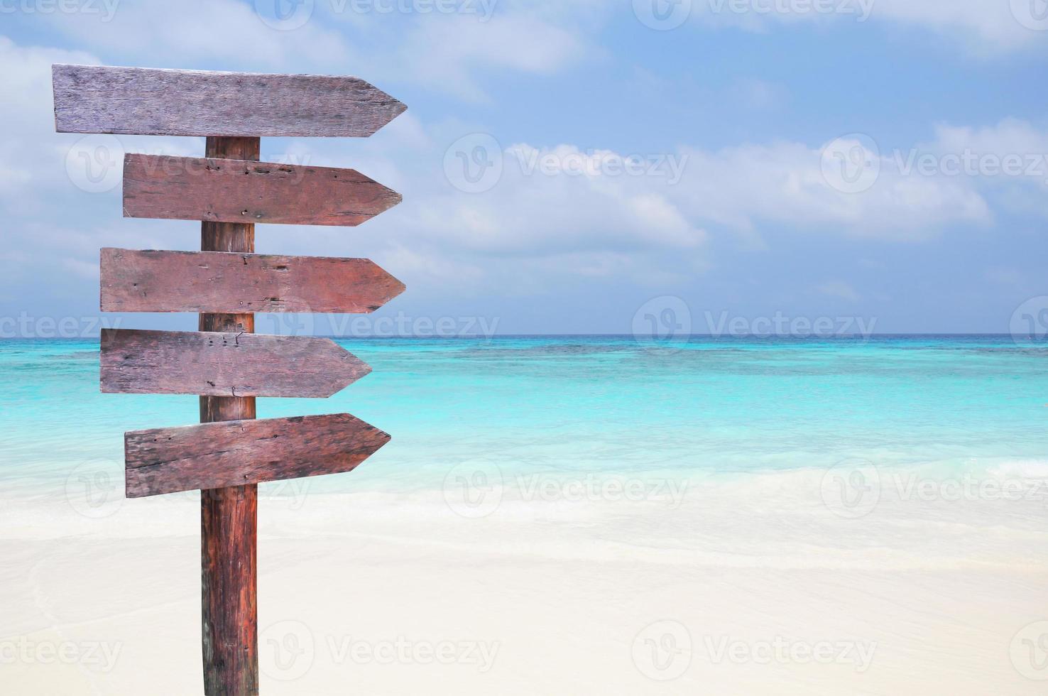 señales de madera para las direcciones de viaje en la playa con fondo de mar y cielo azul. foto