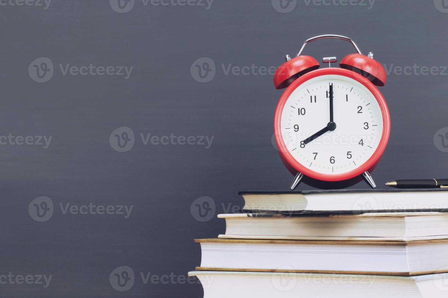 alarm clock red,pen on book, stationery chalk blackboard background. Alarm clock preparation for note and reading book. Education back to school concept. Leave empty copy space for text. photo