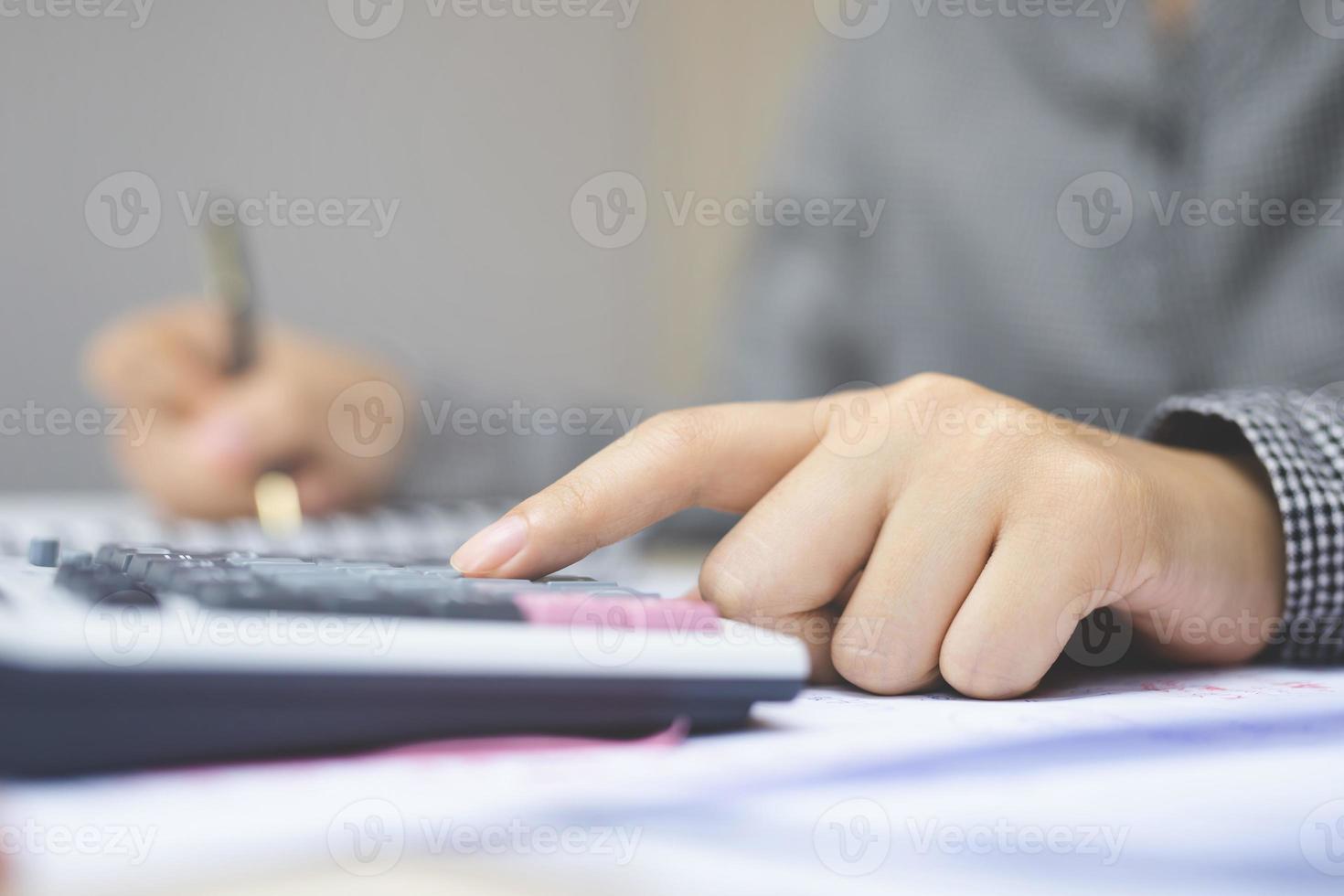 Close up of businesswoman or accountant hand holding pencil working on calculator to calculate financial data report, accountancy document and laptop computer at office, business concept photo