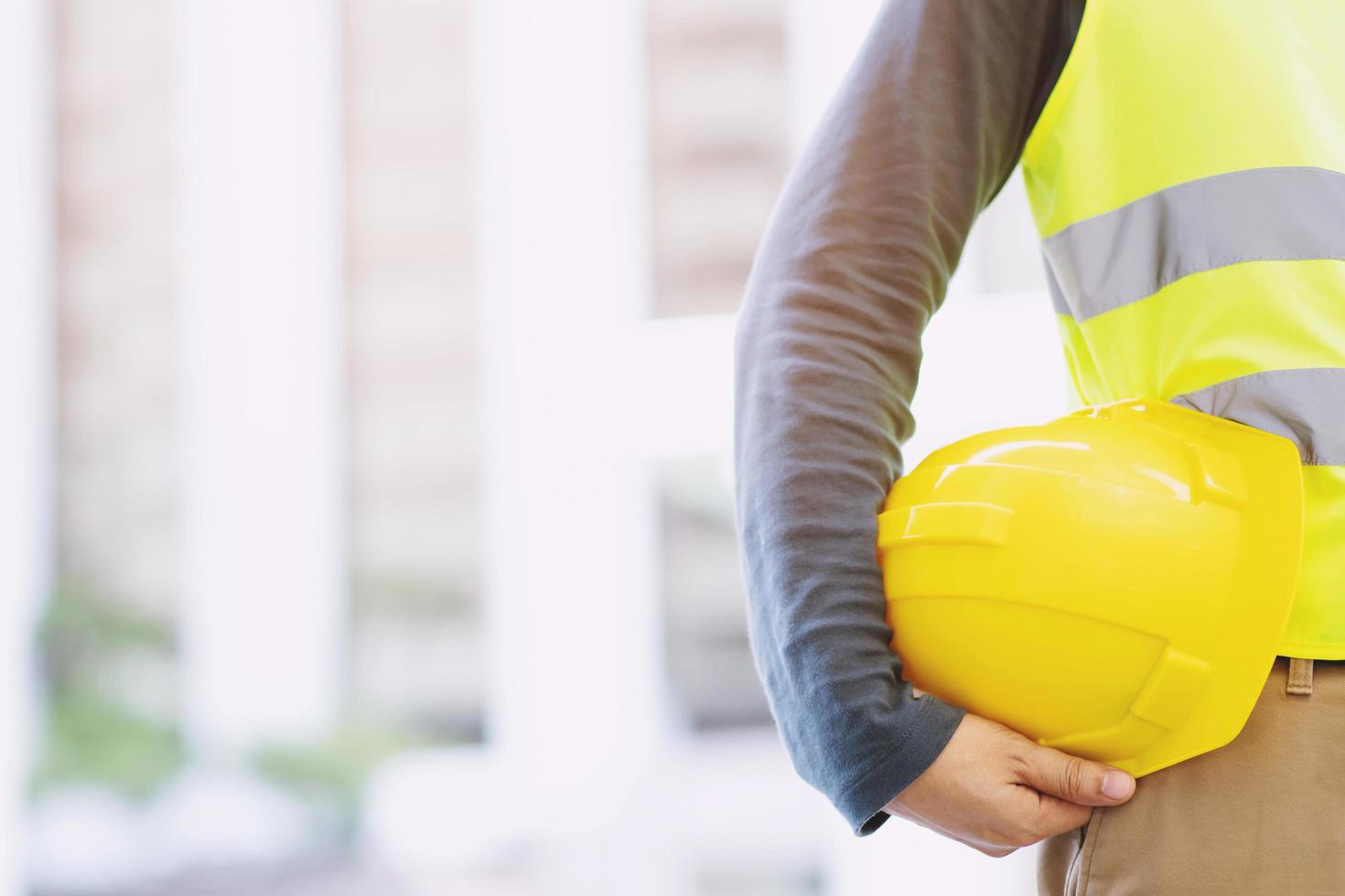 Close up backside view of engineering male construction worker stand holding safety yellow helmet and wear reflective clothing for the safety of the work operation. outdoor of building background. photo