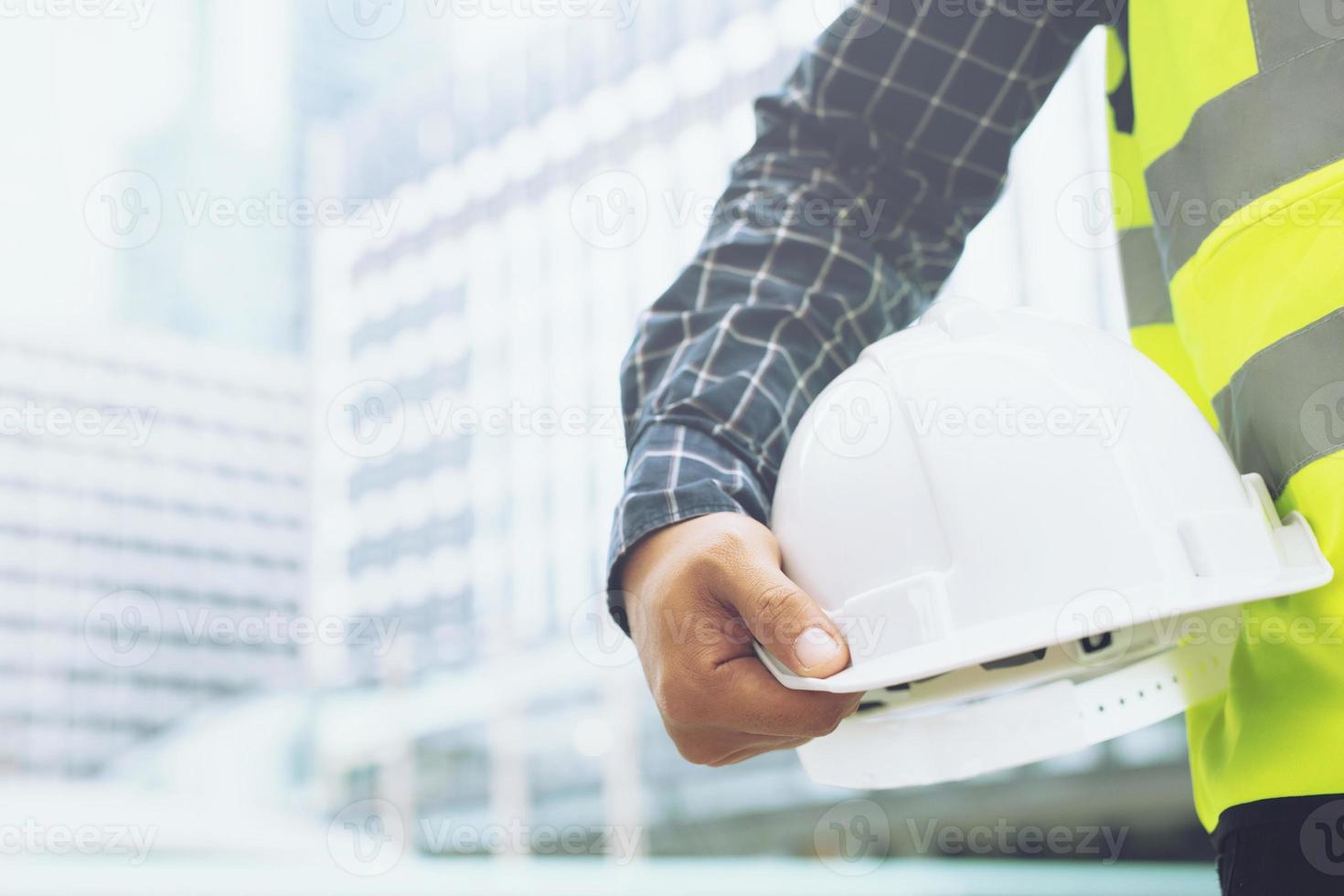 Close up backside view of engineering male construction worker stand holding safety yellow helmet and wear reflective clothing for the safety of the work operation. outdoor of building background. photo