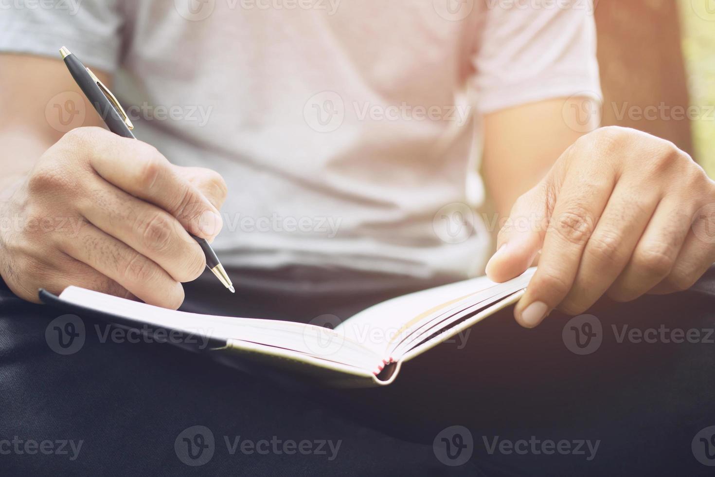 close up hand young woman are sitting on a marble chair. using pen writing Record Lecture note pad into the book in park public. photo