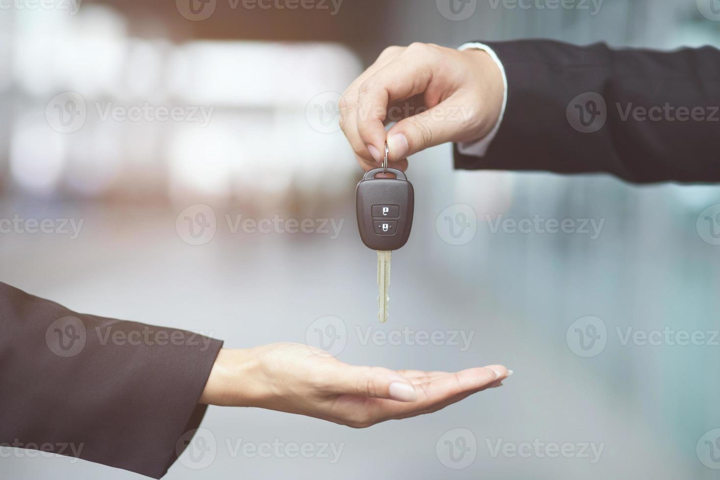 mano de hombre de negocios sosteniendo las llaves del auto al frente con el auto en el fondo. concesionario de transporte y concepto de ventas foto