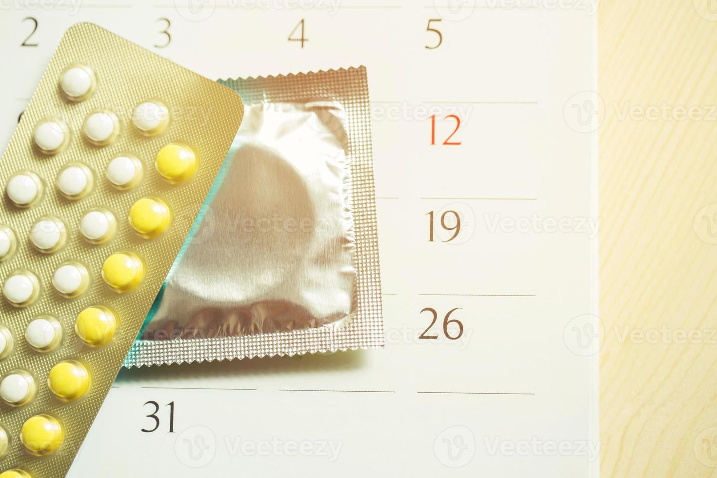 Contraceptive control pills and condom on date of calendar calculate date Control the birth rate. table wood background. health care and medicine, contraception concept. empty space for text. photo