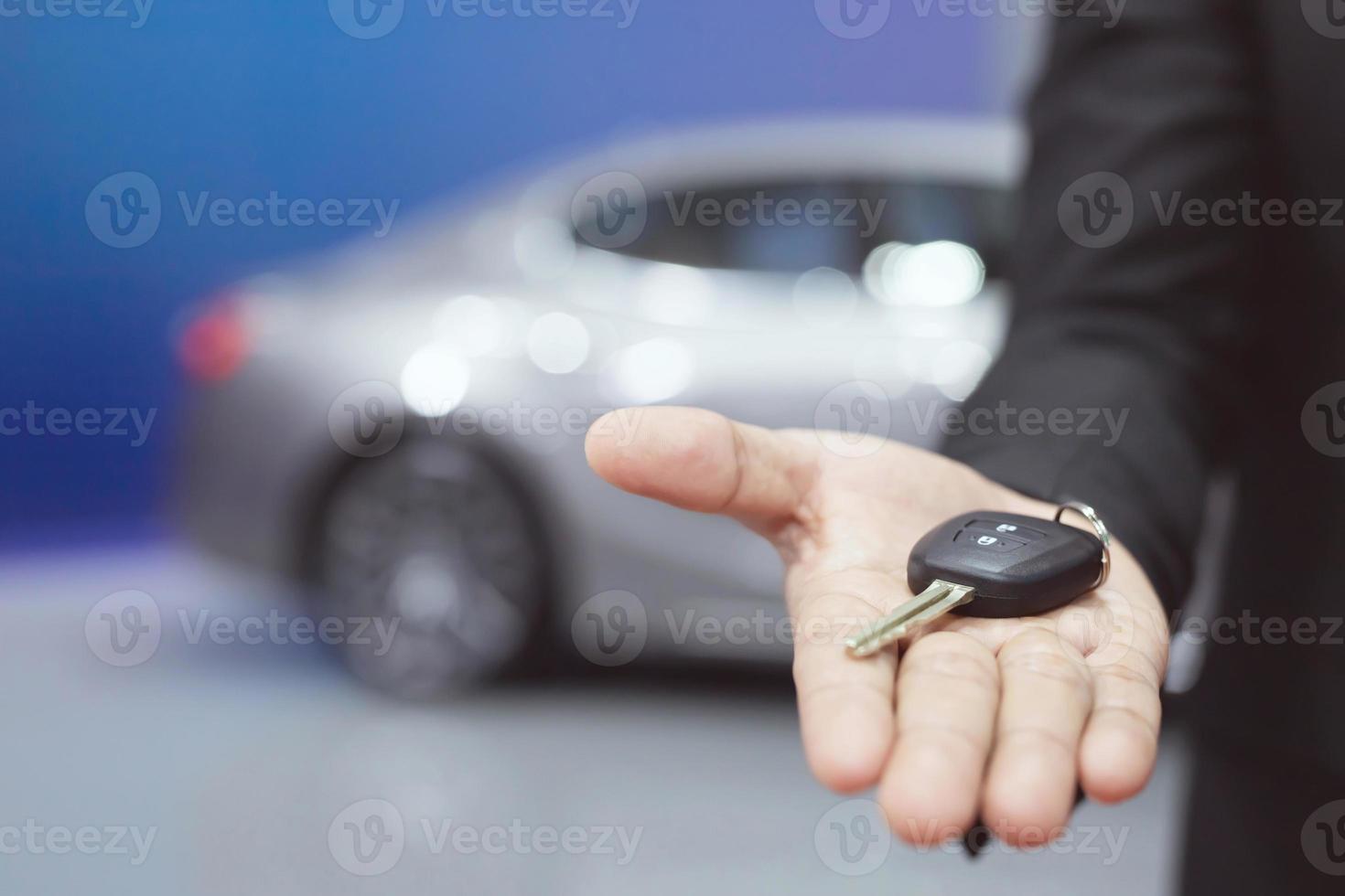 mano de hombre de negocios sosteniendo las llaves del auto al frente con el auto en el fondo. concesionario de transporte y concepto de ventas foto