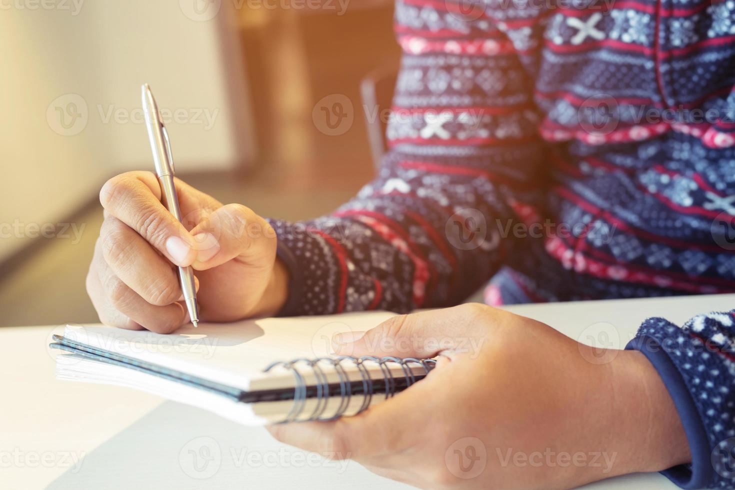 close up hand young man are sitting on a marble chair. using pen writing Record Lecture note pad into the book in park public. photo
