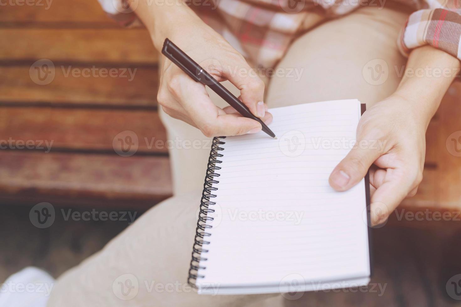 close up hand young man are sitting using pen writing Record Lecture note pad into the book on the table wood. photo