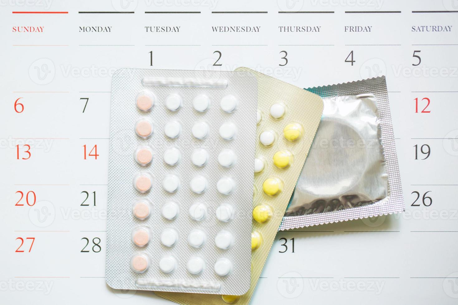 píldoras anticonceptivas y condones en la fecha del calendario calcular la fecha controlar la tasa de natalidad. fondo de madera de mesa. atención médica y medicina, concepto de anticoncepción. espacio vacío para texto. foto