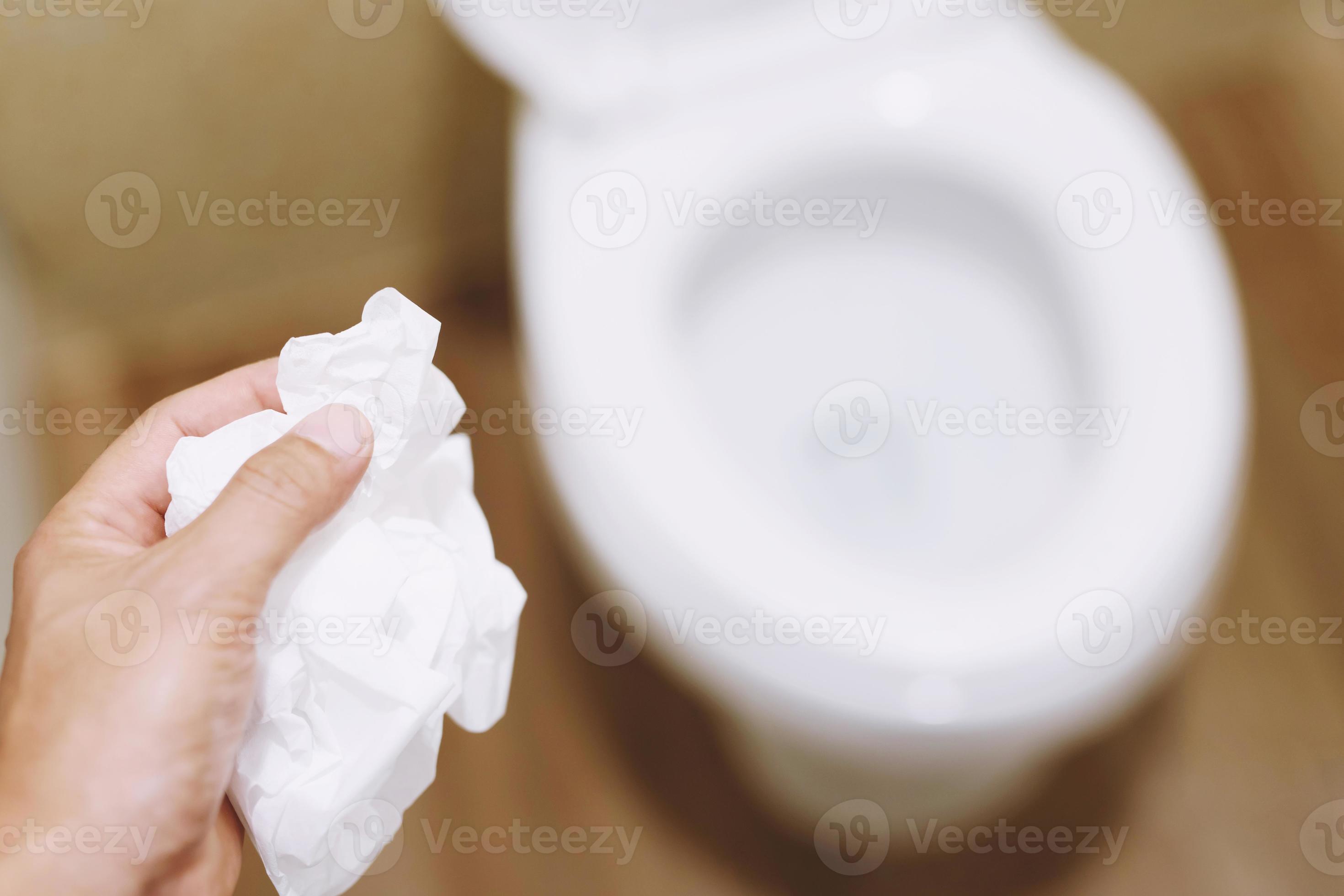 close up hand holding a tissue to be thrown into the toilet bowl. Can
