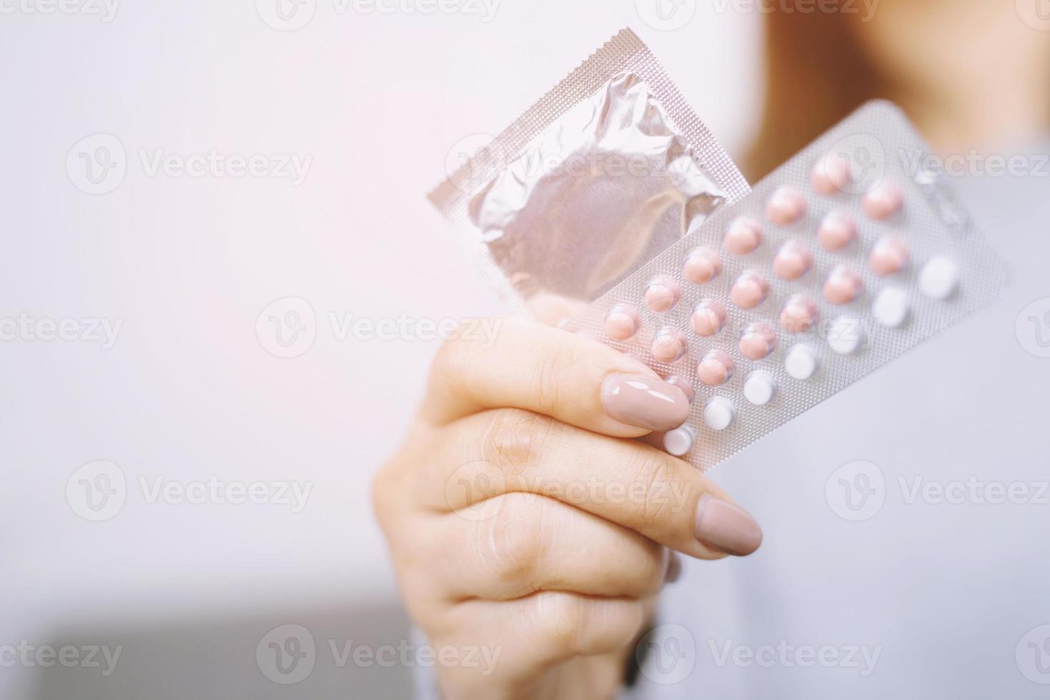 mano de mujer sosteniendo píldoras anticonceptivas y condones en la cama. protección, sexo seguro. concepto de control de la natalidad. copie el espacio foto