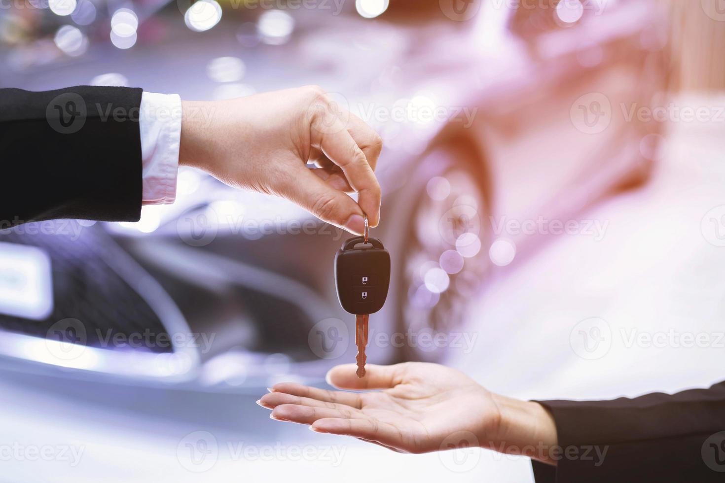 la llave del auto, el hombre de negocios entrega la llave del auto a la otra mujer en el fondo del auto. foto