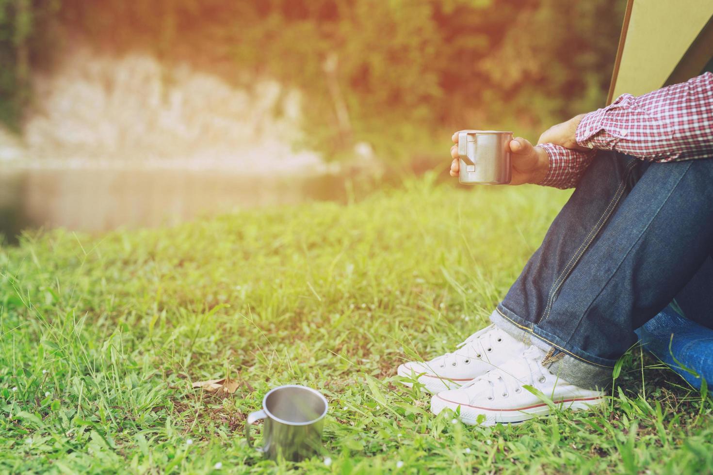 hiking man backpacker sitting front tent camping thirsty man having a break pours water drinking from a steel water bottle.  adventure, travel and tourism concept photo