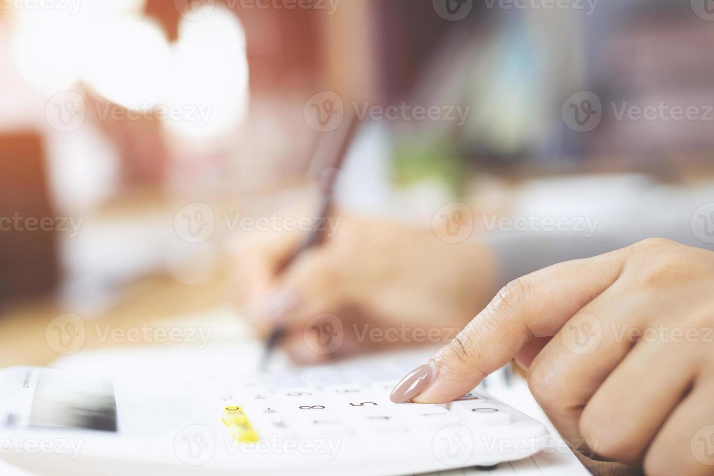 cerrar la mano de una mujer joven está escribiendo en un cuaderno y usando una calculadora contando haciendo notas contables al hacer finanzas en la oficina en casa. concepto de finanzas de ahorro. bloc de notas foto