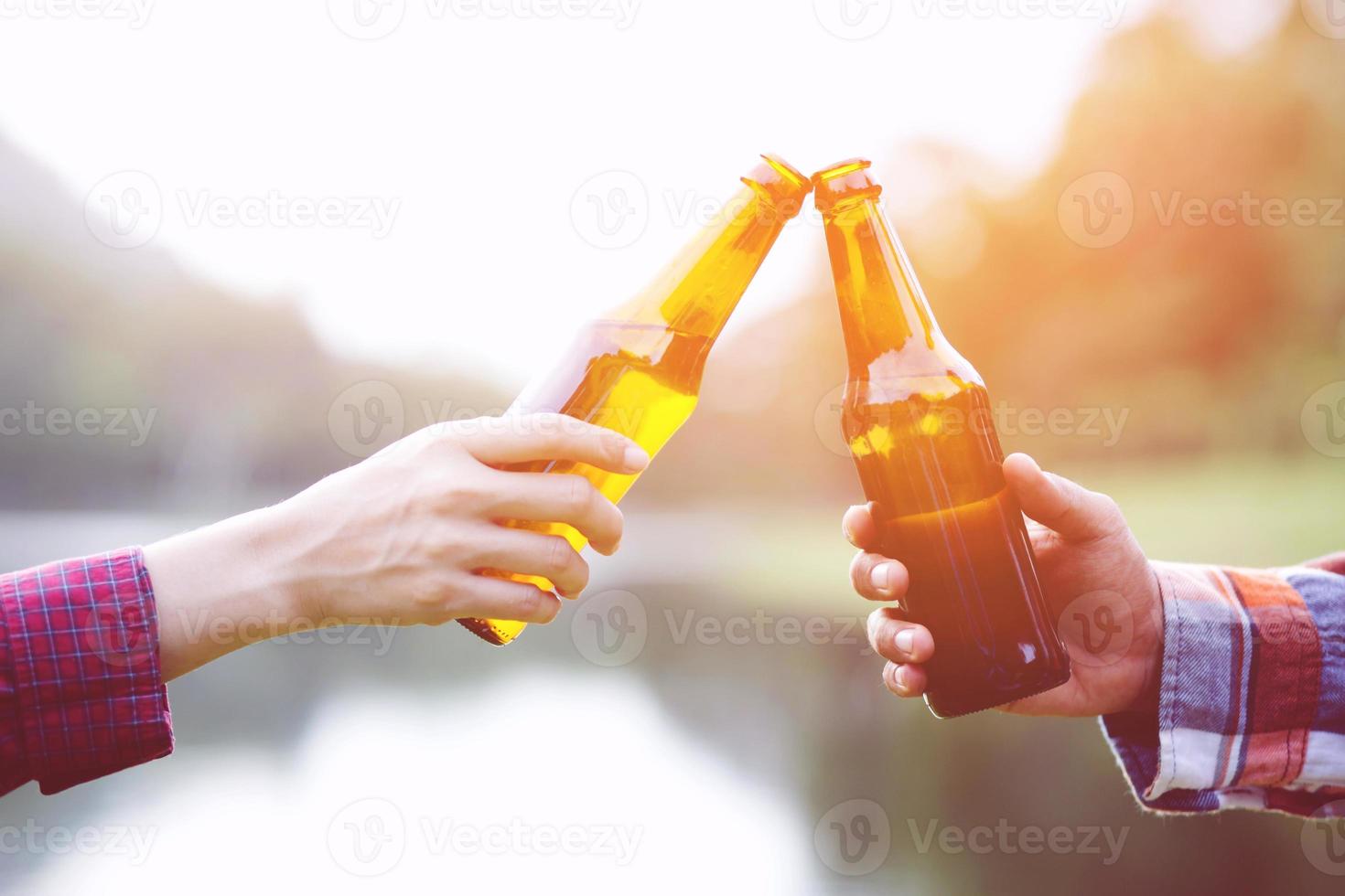 Traveling two young Friends having fun together Relax in hiking camp  and drinking beer Cheers bottles And Enjoying. Vacation Travel Adventure Concept. mountain forest river view background. photo