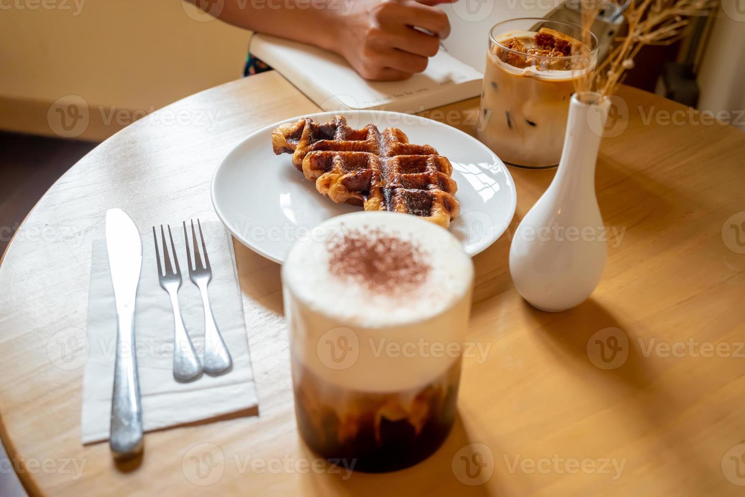 A Sunday morning meal in cafe, two cups of coffee, honey latte and Eispanner americano served with waffle on plate, decorated with with vase. photo