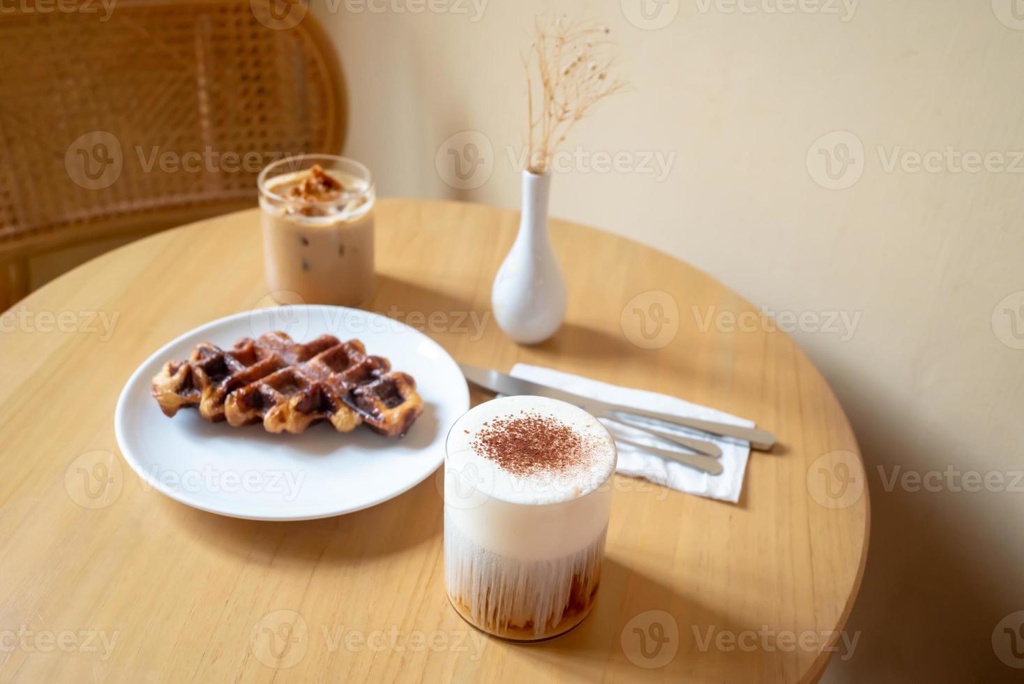 A Sunday morning meal in cafe, two cups of coffee, honey latte and Eispanner americano served with waffle on plate, decorated with with vase. photo