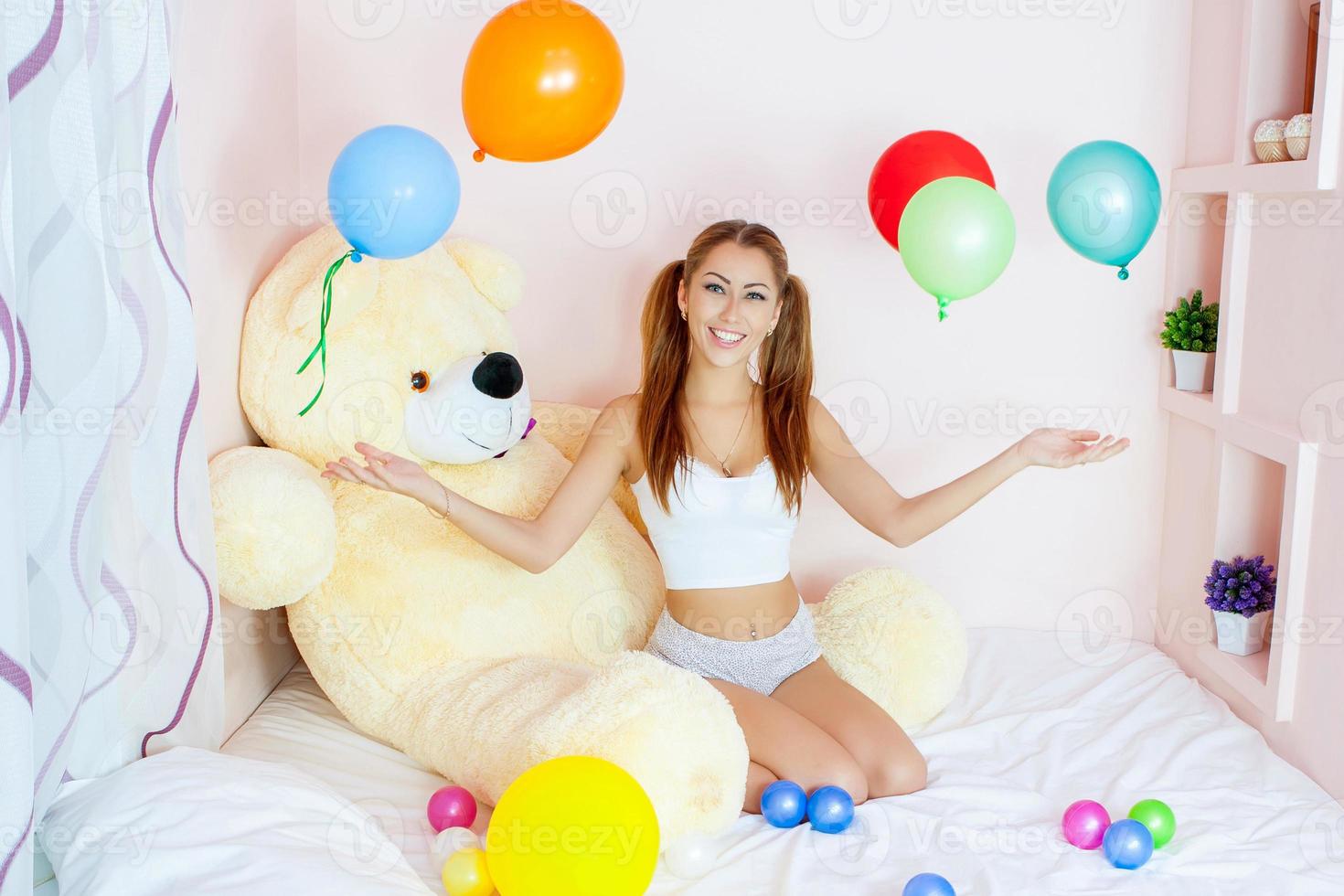 mujer en la cama con gran oso de juguete y bolas de colores. foto