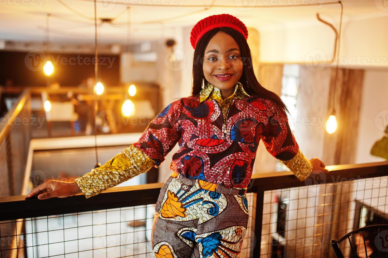 Enthusiastic african american woman in trendy coloured outfit with red beret chilling in cozy cafe. photo