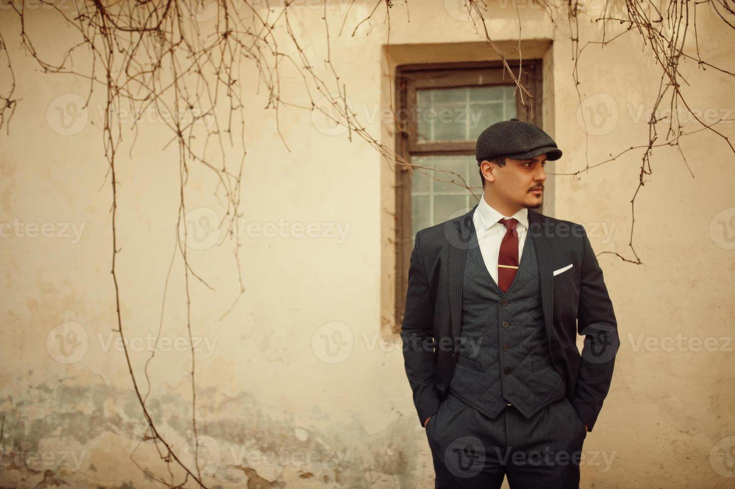 Portrait of retro 1920s english arabian business man wearing dark suit, tie and flat cap. photo