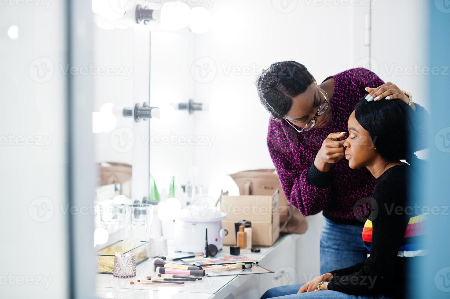 African American woman applying make-up by make-up artist at beauty saloon. photo