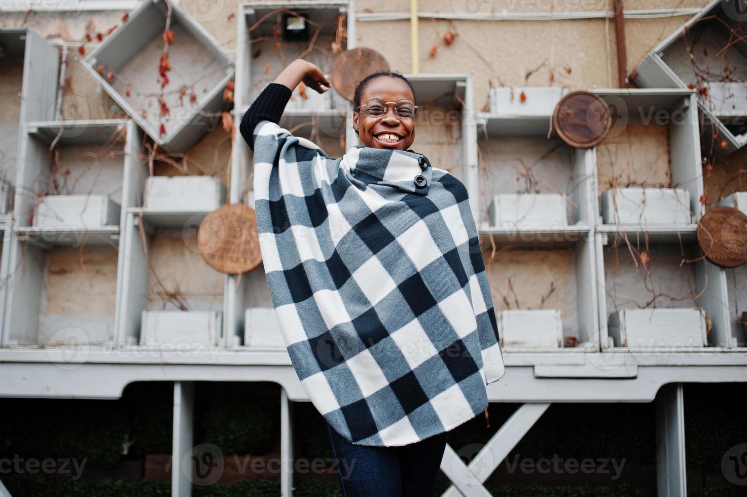 African woman in checkered cape and eyeglasses posed outdoor. photo