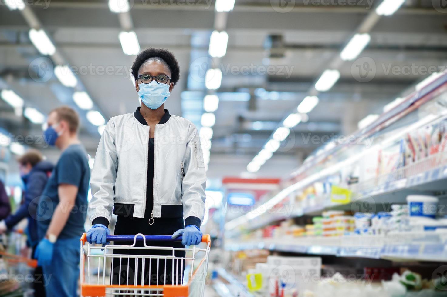 mujer africana con máscara médica desechable y guantes comprando en un supermercado durante el brote de pandemia de coronavirus. tiempo de epidemia. foto