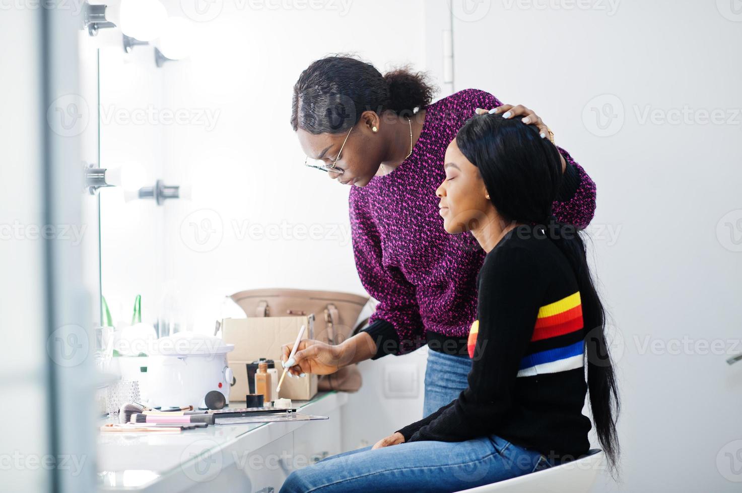 African American woman applying make-up by make-up artist at beauty saloon. photo