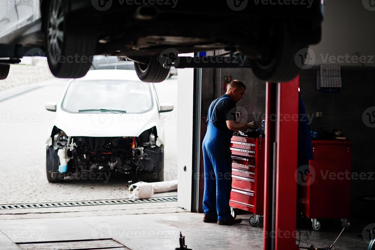 Car repair and maintenance theme. Mechanic in uniform working in auto service. photo