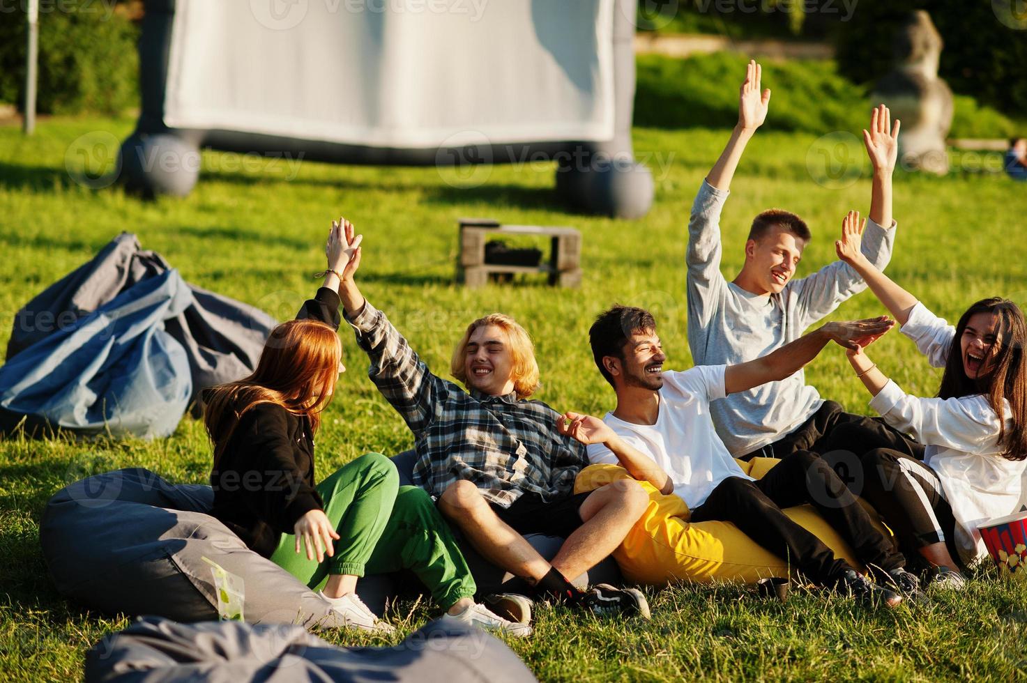 Young multi ethnic group of people watching movie at poof in open air cinema. photo