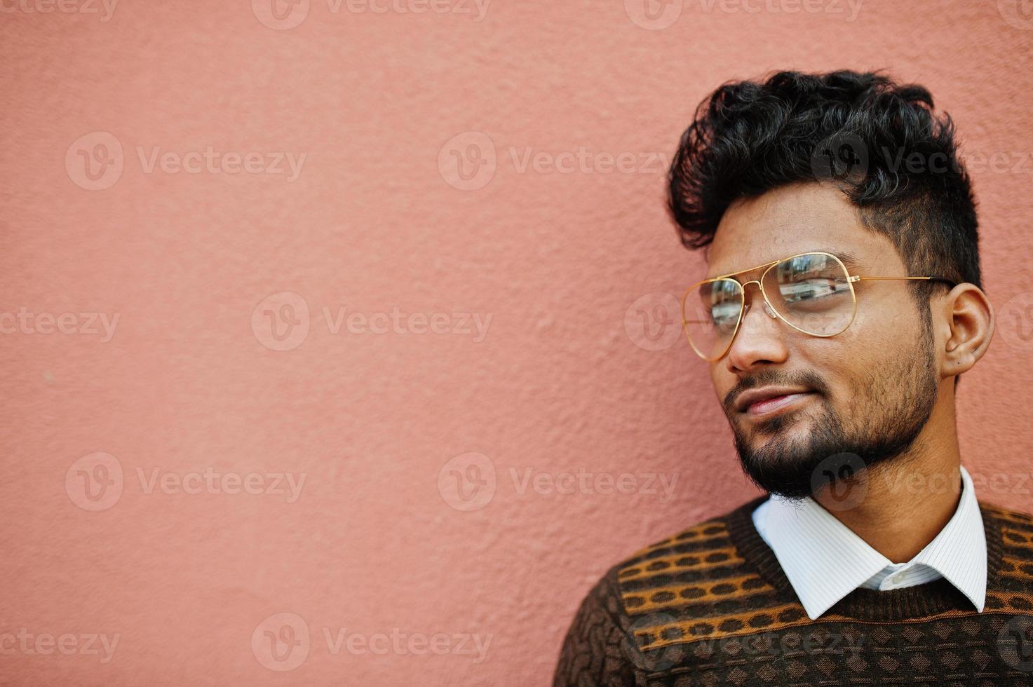 Portrait of young stylish indian man model in eyeglasses isolated on pink wall background. photo