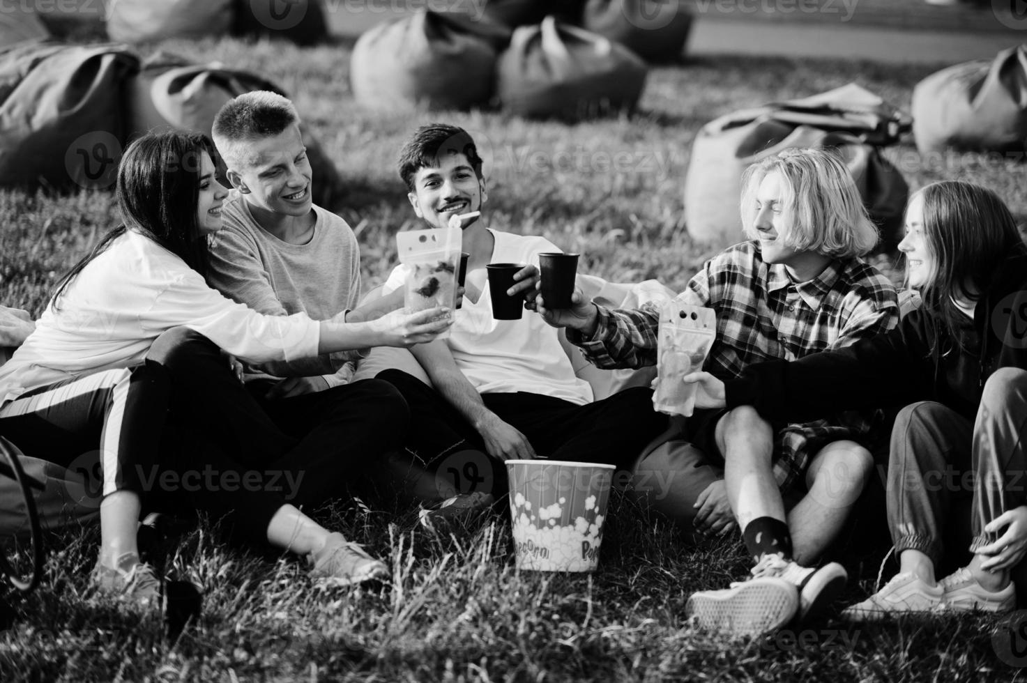 Young multi ethnic group of people watching movie at poof in open air cinema and drinking. photo