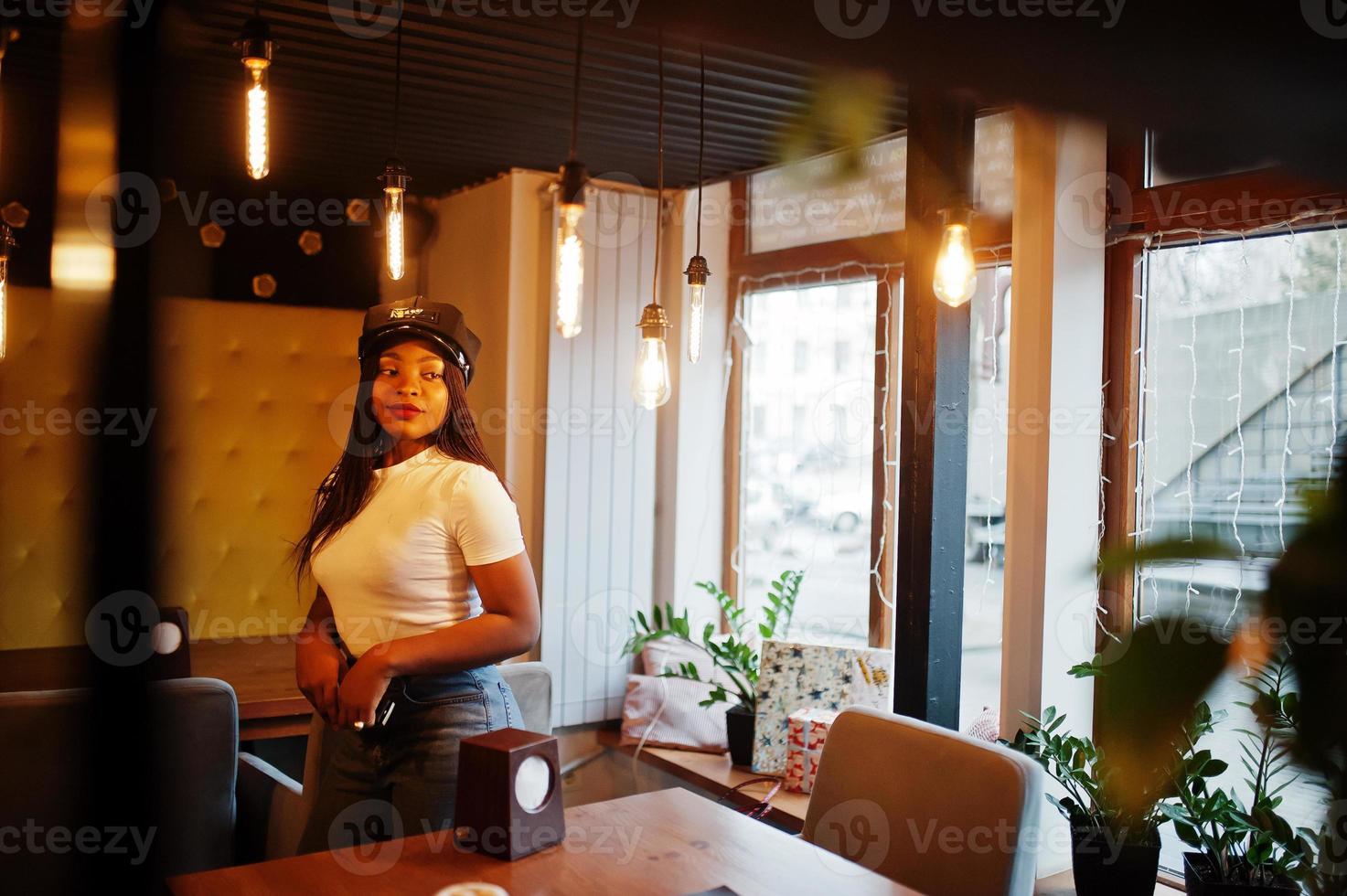 Fashionable african american woman in black cap chilling in cozy cafe. photo