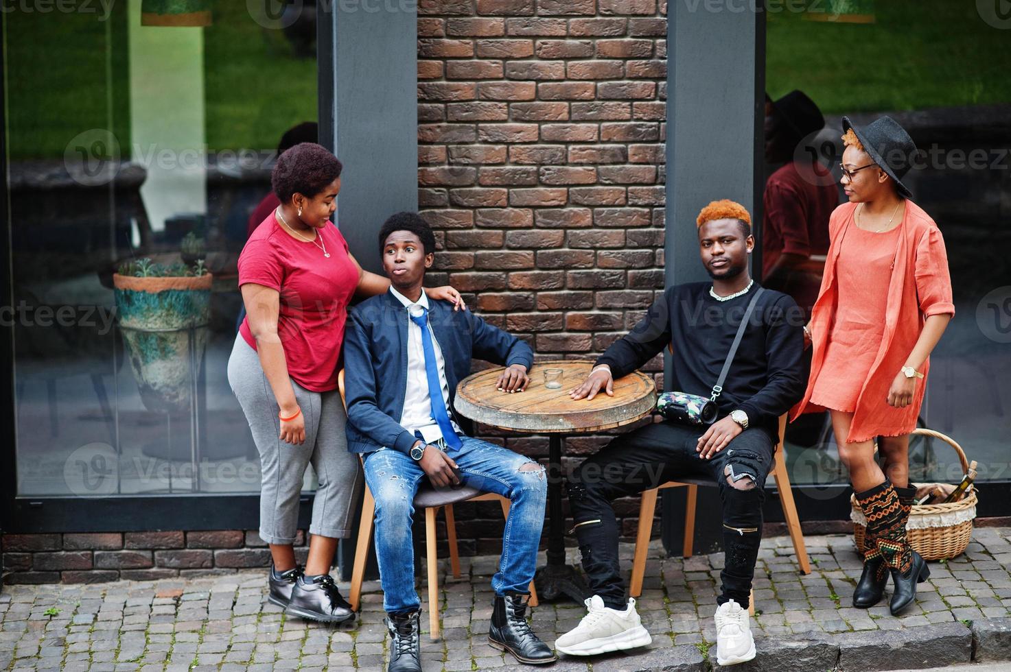Four african friends sit by table in outdoors cafe. Two black girls with guys. photo