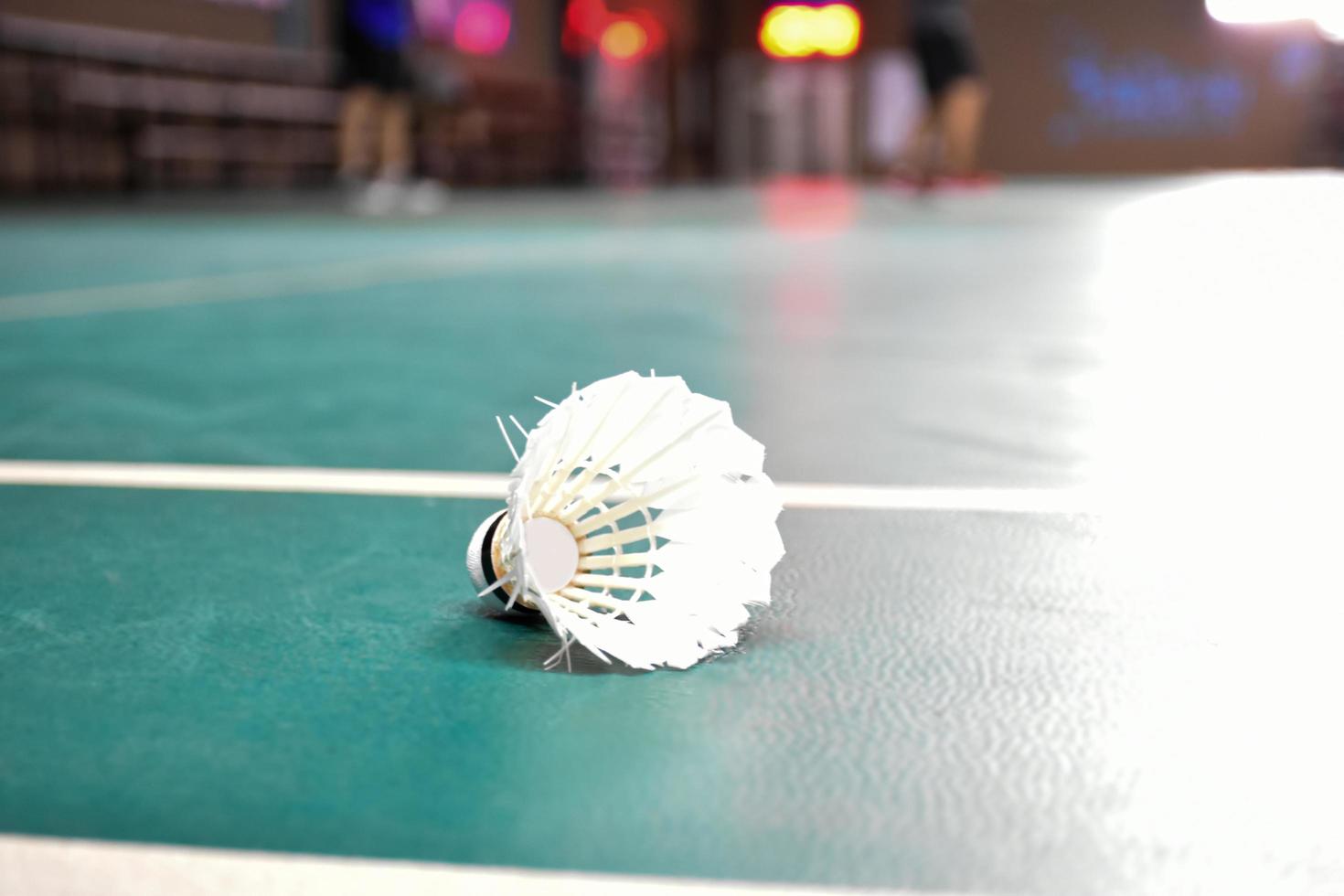 Cream white badminton shuttlecock and racket with neon light shading on green floor in indoor badminton court, blurred badminton background, copy space. photo