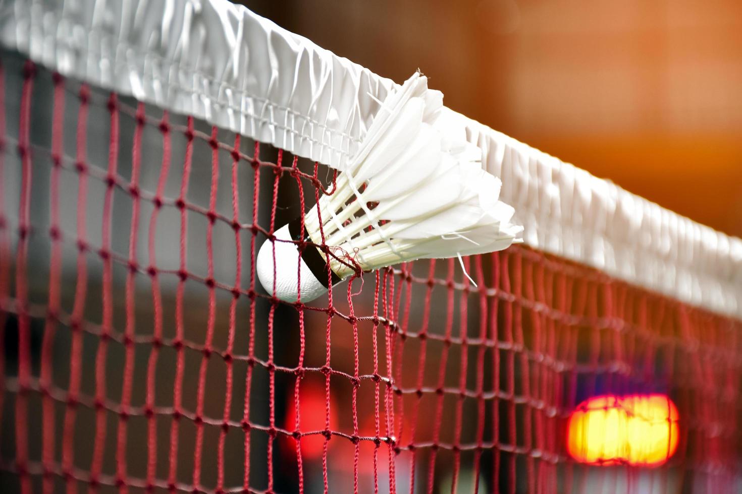 Cream white badminton shuttlecock and racket with neon light shading on green floor in indoor badminton court, blurred badminton background, copy space. photo